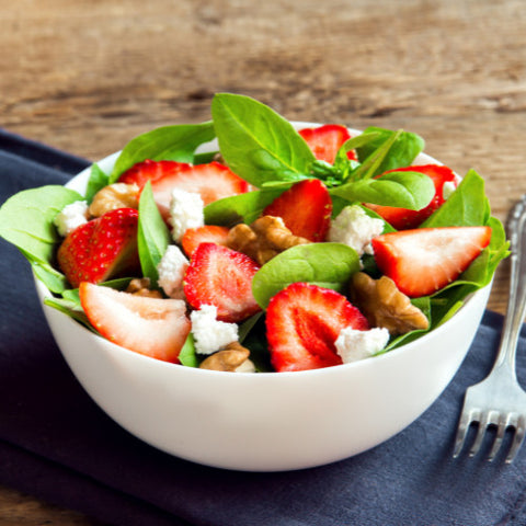 strawberry, spinach, feta, and walnut salad in a white bowl.