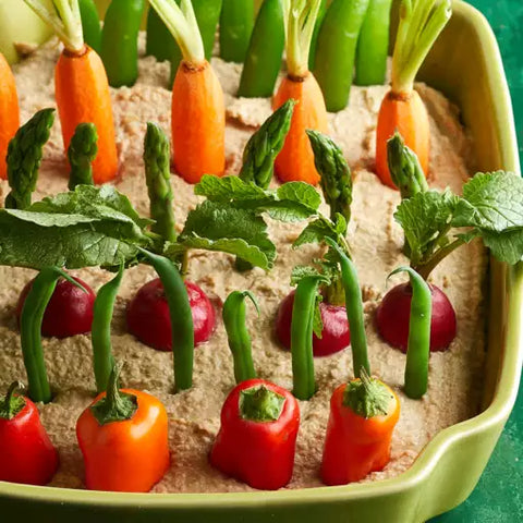 various vegetables sticking out of hummus to make it look like a garden.