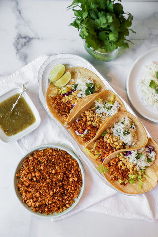 plate of 4 quinoa and tofu tacos sitting next to various toppings on a marble table