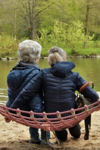 two women sitting in a hammock beside a river