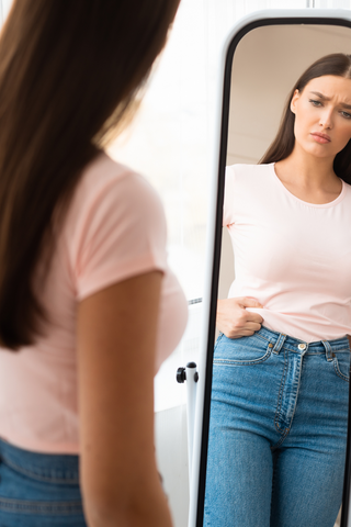 a woman standing in front of a mirror examining her waistline