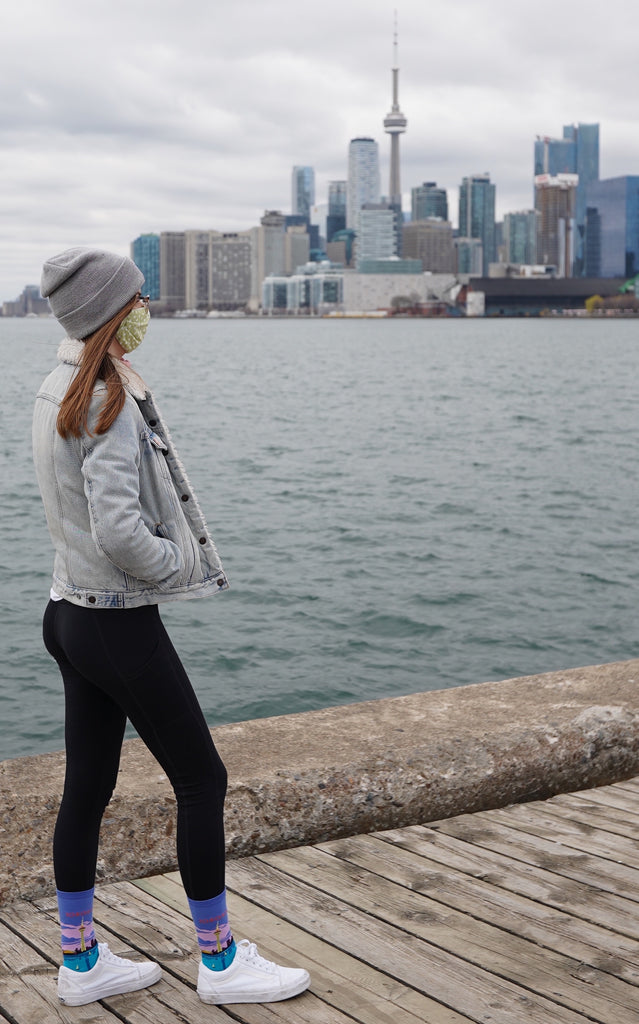 Woman looks out at Toronto harbourfront and skyline with CN Tower, wearing black leggings with Toronto themed socks