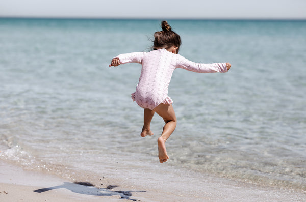 Girl jumping at beach wearing Willow Swim Sophia embroidery swimsuit