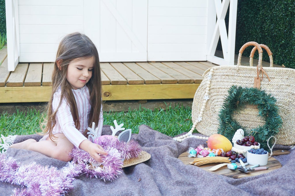 Little girl in garden with picnic decorating christmas hat wearing Willow Swim kids swimwear