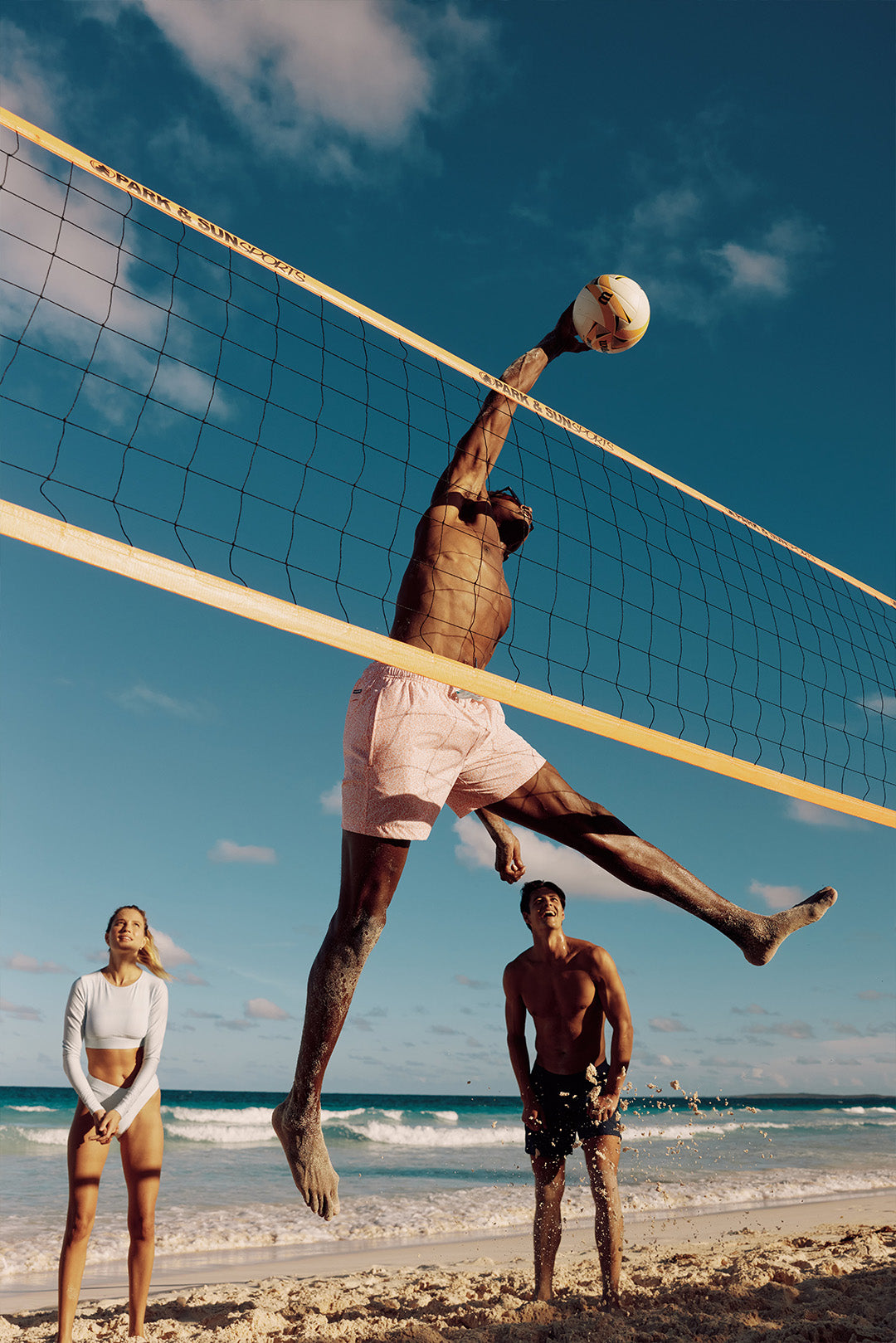 Man playing beach volleyball wearing preppy pink swim trunks.