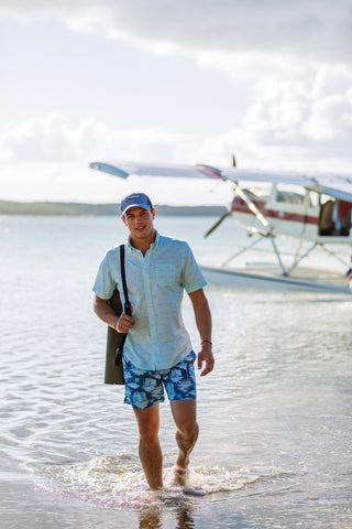 guy standing on beach wearing short sleeve button down and swim trunks