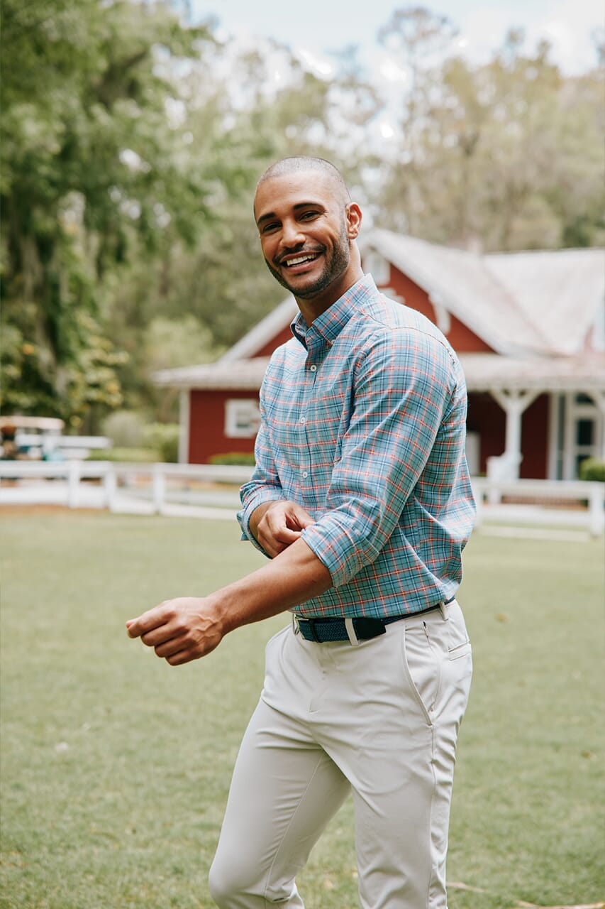 Man wearing plaid button up shirt with khaki chino pants in a green field.