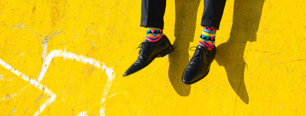 image of Low-Section-Of-Man-Wearing-Shoes-While-Sitting-On-Yellow-Wall