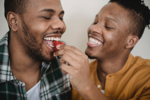 A man feeding a strawberry to another man