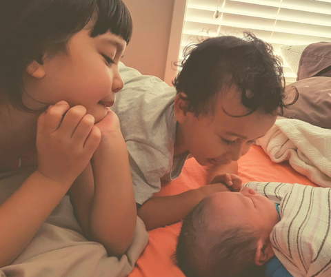A picture of 3 kids. A girl and boy looking lovingly at a newborn baby. 