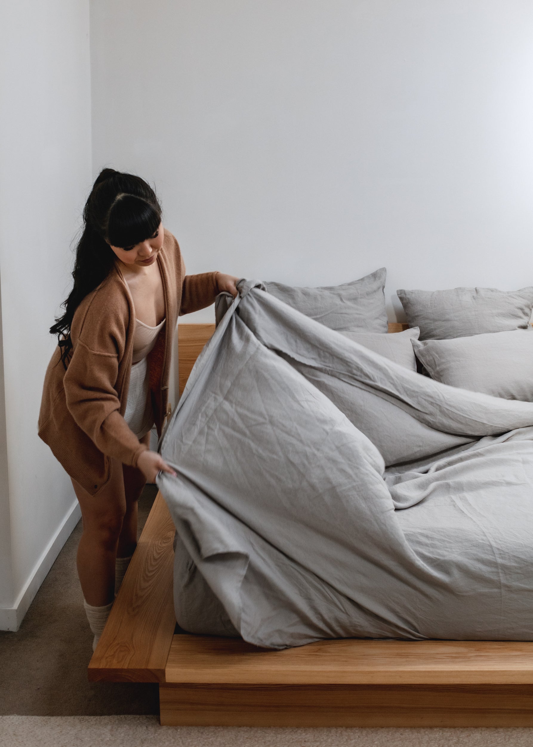 A woman making her bed with Flax Home linen sheets in the fall.