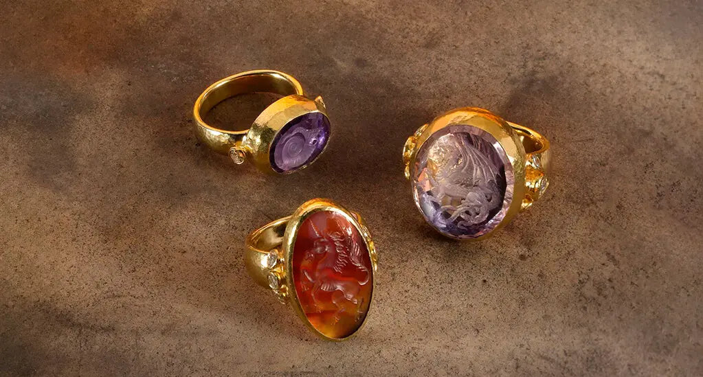 A lady in a black dress accessorized with gold jewelry, including a handcrafted bracelet featuring mixed stones, micro mosaics, ancient coins, and a lava cameo from the Antiquities Collection.