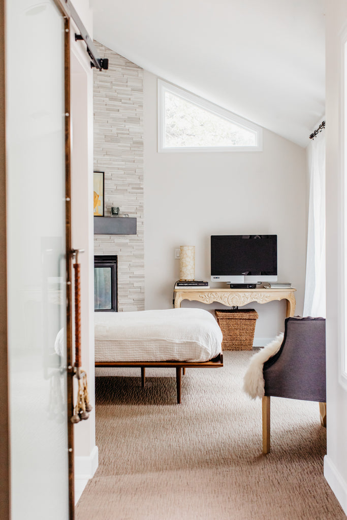 Warm modern bedroom with light grey stone fireplace and raised walnut bed.