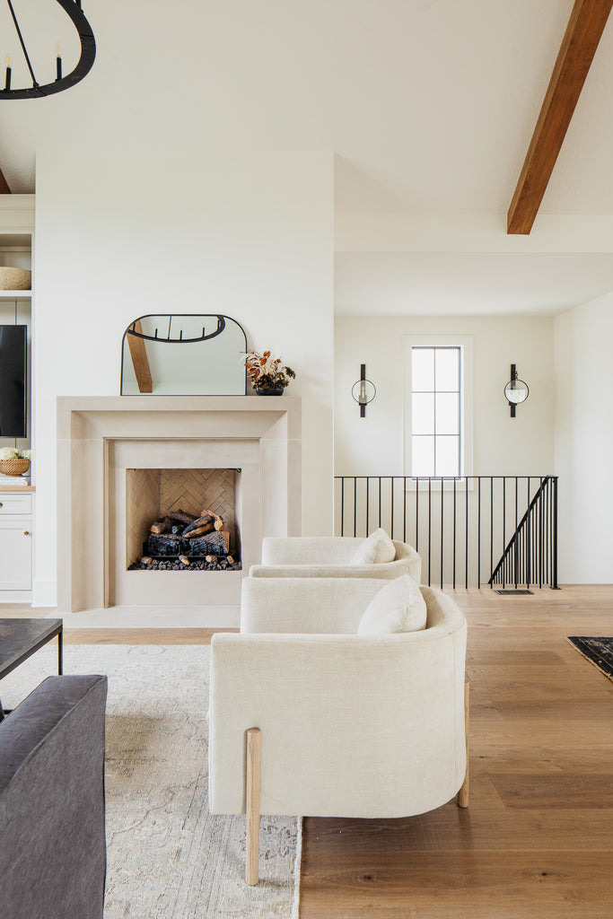 Limestone fireplace with black sconces, vintage persian rug, verellen sullivan chairs and arched target mirror.