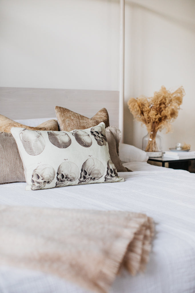 Master bedroom with whitewashed wood canopy bed, pom pom linen bedding, iron cushioned chairs, and vintage persian rug.