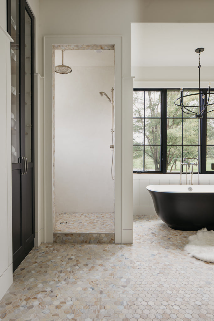 Salle de bain principale avec baignoire noire, fenêtres noires et sol en marbre.