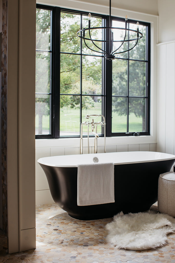 Salle de bain principale avec baignoire noire, fenêtres noires et sol en marbre.