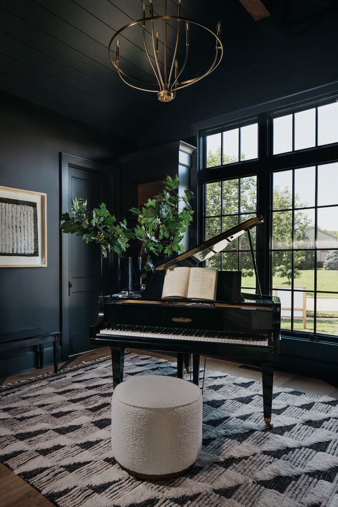 Moody piano music study with dark green walls, Moroccan rug, and black windows.