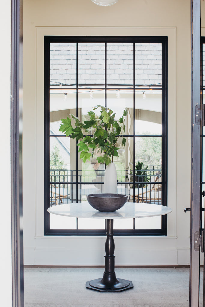 Entry with round marble table with black windows and warm wood floors.