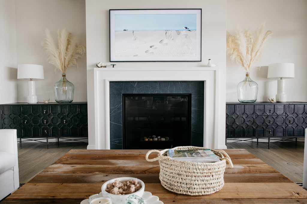 We love the client's selection of bluestone for the fireplace flanked with white molding. The precious black Dovetail cabinets, creamy white pampas grass in recycled glass vases, and white hand-glazed ceramic Tory lamps from Arteriors give the living room a warm and beachy vibe.