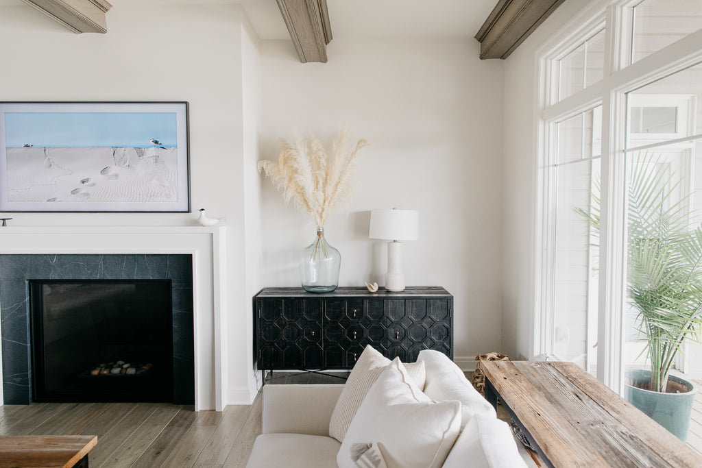 We love the client's selection of bluestone for the fireplace flanked with white molding. The precious black Dovetail cabinets, creamy white pampas grass in recycled glass vases, and white hand-glazed ceramic Tory lamps from Arteriors give the living room a warm and beachy vibe.