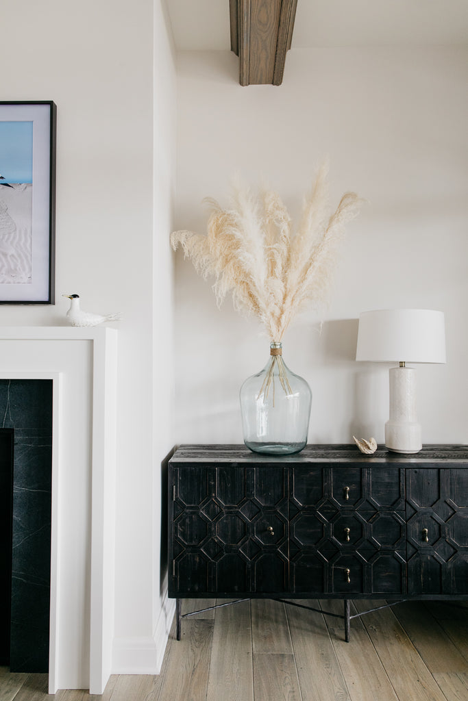 The precious black Dovetail cabinets, creamy white pampas grass in recycled glass vases, and white hand-glazed ceramic Tory lamps from Arteriors give the living room a warm and beachy vibe.