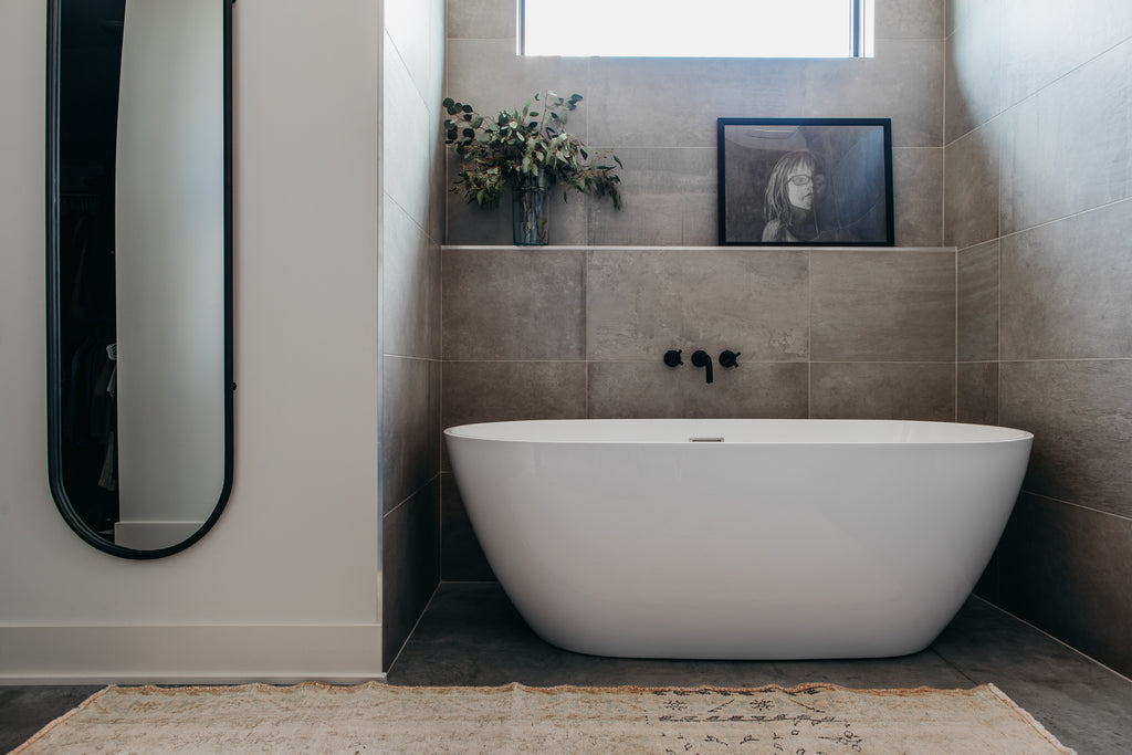 Salle de bain principale de type spa avec miroir en fer de forme ovale, tapis sable et baignoire blanche.