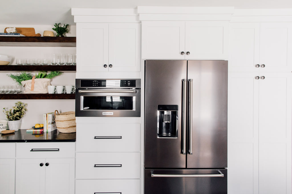 The custom-built open shelving in the kitchen is such a fun contrast to the cabinets. This is such a gorgeous way to show off cute ceramic and glassware along with seasonal decor and flowers. Love the convention KitchenAid microwave and oven black stainless steel appliances! Makes cooking so much more fun!