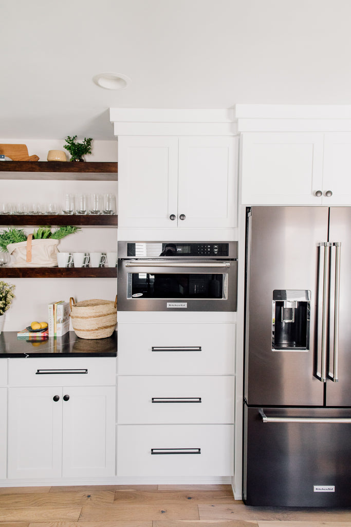 The custom-built open shelving in the kitchen is such a fun contrast to the cabinets. This is such a gorgeous way to show off cute ceramic and glassware along with seasonal decor and flowers. Love the convention KitchenAid microwave and French-door fridge in black stainless steel! Makes cooking so much more fun!