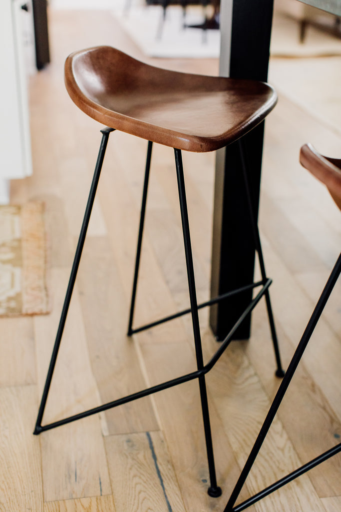 The fabulous Equestrian counter stool's leather seat visually floats against the black island in a blend of utilitarian and rustic design.