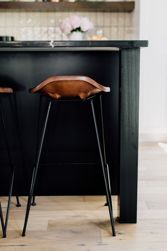 The fabulous Equestrian counter stool's leather seat visually floats against the black island in a blend of utilitarian and rustic design.