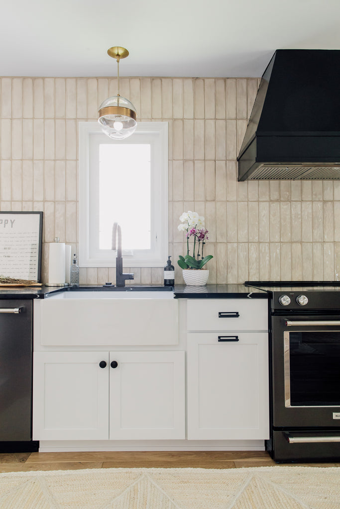 The beautiful apron front sink, the gorgeous Garrison Round Pendant, beige tiles, and fun window to the garden are one of our favorite moments in this kitchen remodel.