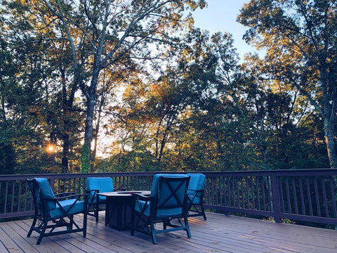 metal chairs and a table in a deck with large green trees surrounding them