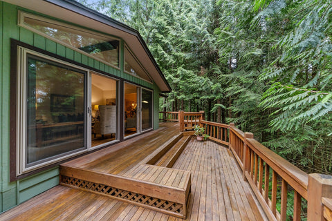 a green house with a wooden deck facing a forest