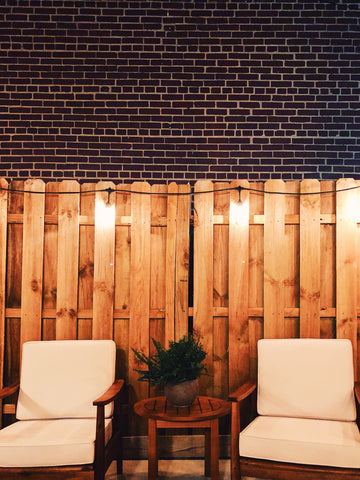 two white chairs in a patio with lights and wooden fences