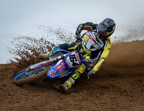 Motocross rider entering a sandy corner keeping the elbows up to stabilize the body, sticking insode foot out towards front wheel to add weight to the front end for traction and stability, and keeping the outside foot on the balls of the feet on the peg to keep weight on the outside of the foot.