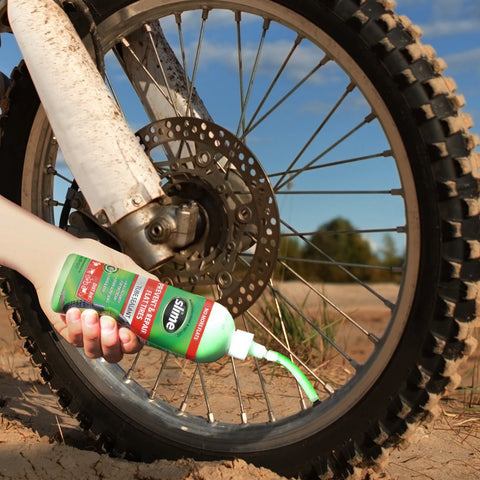 Slime being put into a dirt bike tire. The slime bottle has a tub that screws into the schraider valve of the tube/tire and you can squeeze the bottle to easily fill the tire with sealant.