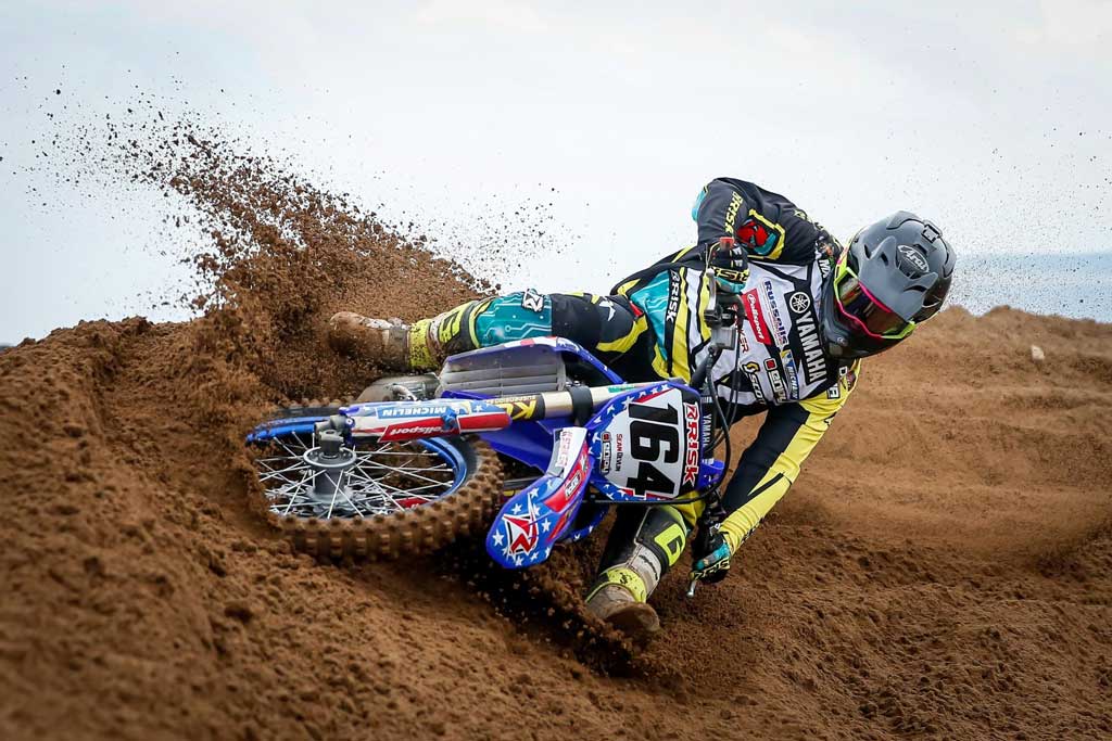 164 motocross racer turning hard into a burm corner wearing full risk racing mx gear including jersey pants and gloves