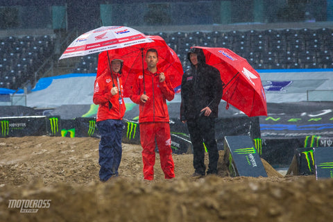 Motocross team taking a track walk in the rain holding umbrellas to get an understanding of the track conditions, track features, and technique for riding it as fast as possible.