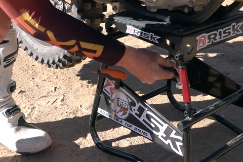 Operating the adjustment bolts while working on their dirt bike on the A.T.S. Stand