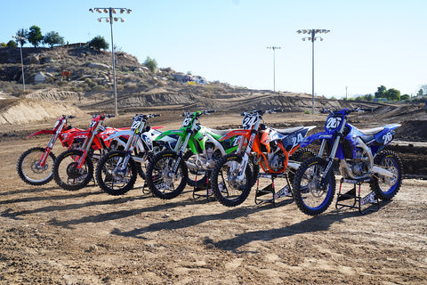 yamaha, ktm, kawasaki, husqvarna, honda, and gas gas lined up in a row for comparison. All bikes sit atop Risk Racing A.T.S. Stands.