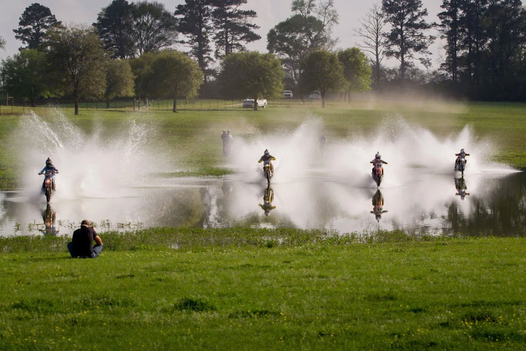 four dirt bikers skipping across a pond at high speeds