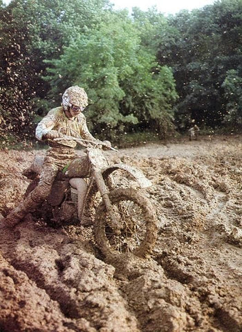 Vintage motocross bike and motocross rider riding through deep mud ruts 