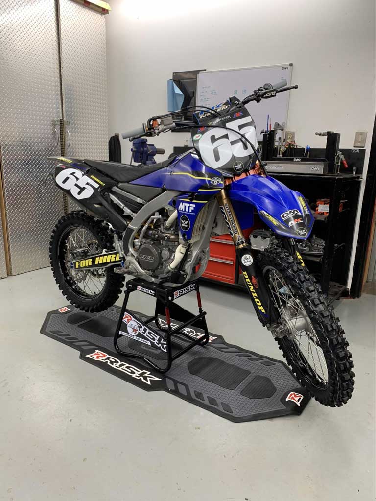 #65 blue dirt bike in a garage sitting on Risk Racing's ATS MX stand and pit mat