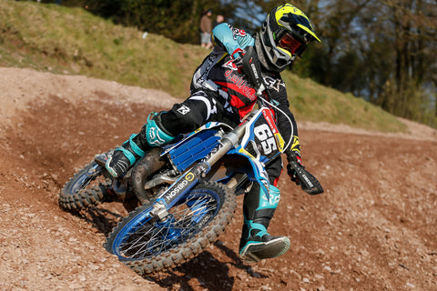 Rider in a rocky corner wearing risk racing's red/teal ventilate v2 series gear.