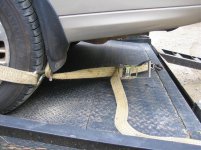 Two ratchet straps hooked to the rear drivers side wheel of a suburban on a flat bed trailer. The ratchet straps are securing the vehicle to the flat bed for transport. 