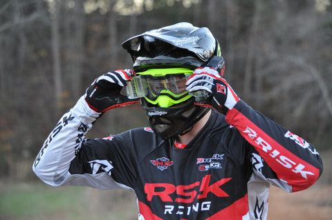 Motocross rider putting the lime green J.A.C. V3 Roll-Off Goggles paired with the ripper automatic roll-off system onto their head before riding
