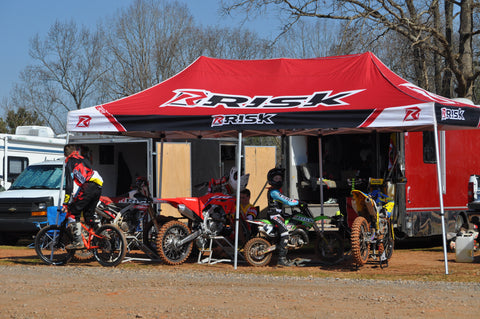 Carpa Risk Racing instalada en una pista de motocross con 4 motos de cross debajo.