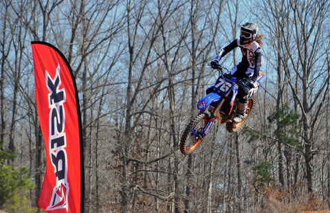 Motocross rider training. Rider is mid air flying by a risk racing feather flag.