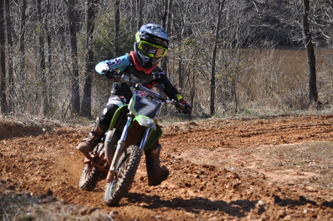 Joven piloto de motocross demostrando buena forma y encontrando la línea más rápida en una curva. Los codos están levantados, el pie interior está delante de la rueda delantera y el pie exterior está sobre la clavija.